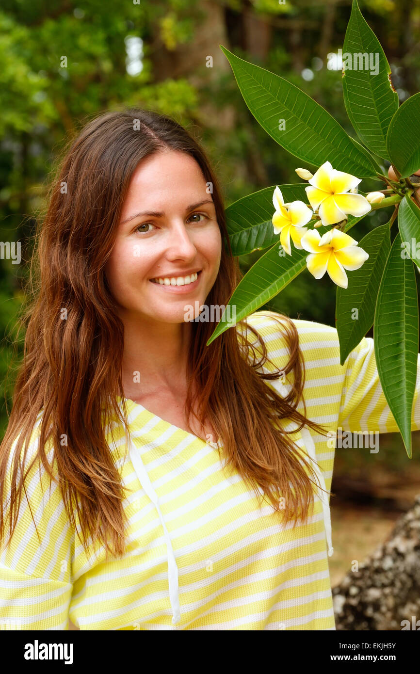 Young woman standing by plumeria arbre jaune Banque D'Images