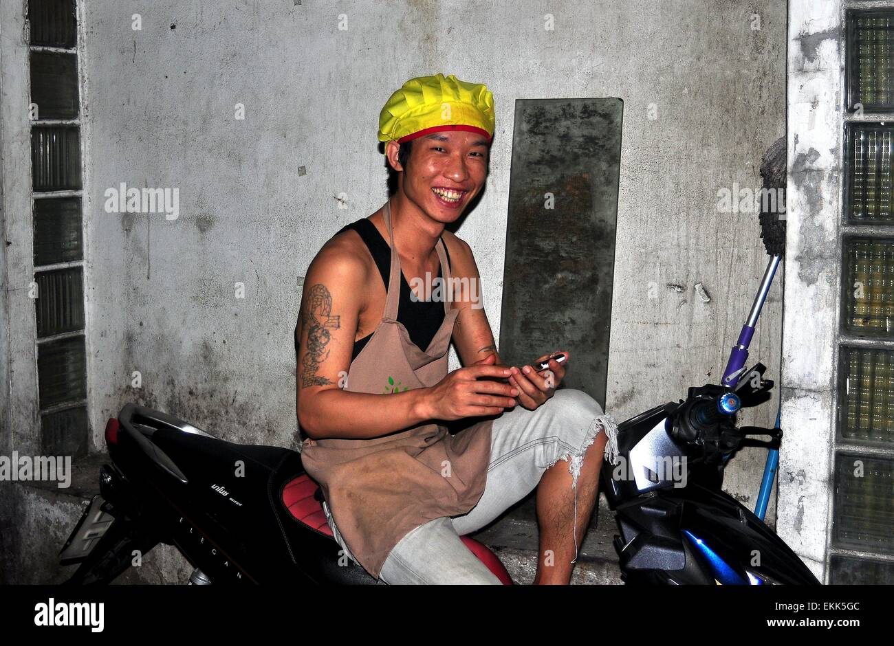 Bangkok, Thaïlande : Thai man avec tatouages bras assis sur sa moto avec son téléphone cellulaire Banque D'Images