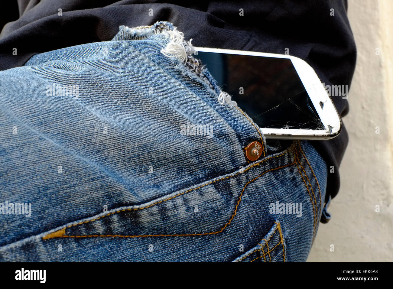 Smart phone avec écran fissuré accroché précairement sur une poche de jeans Banque D'Images