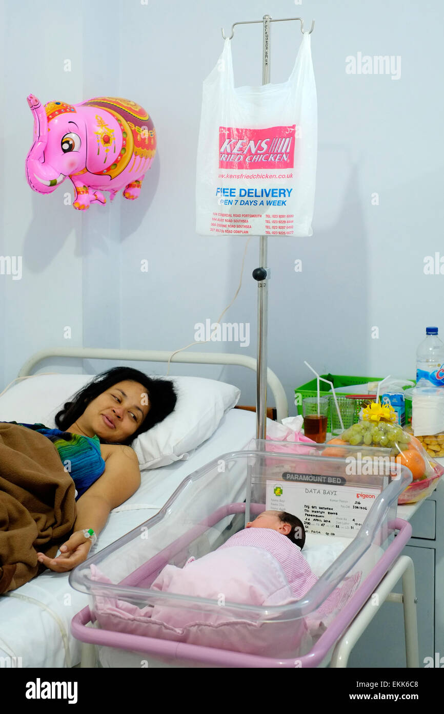 Regarde fièrement ses mère fille nouveau-né à partir de son lit d'hôpital dans le service de maternité Malang, Indonésie Banque D'Images