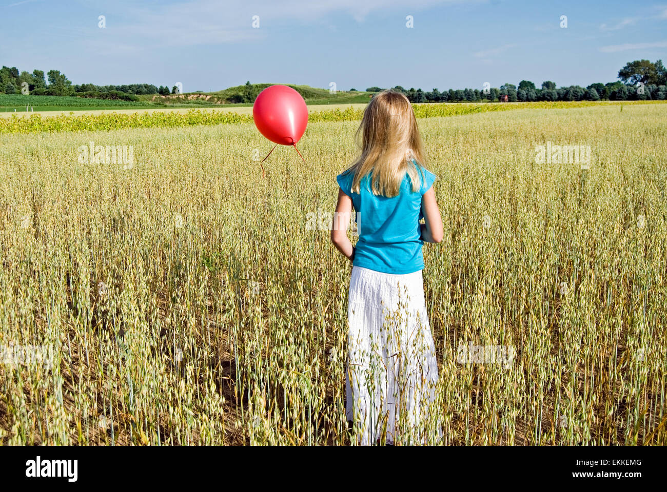 Petite fille avec un ballon rouge dans un champ de blé. Banque D'Images