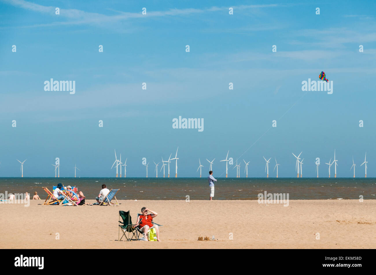 Les familles se détendre et un homme voler un cerf-volant sur la plage de skegness et les éoliennes dans l'arrière-plan Banque D'Images