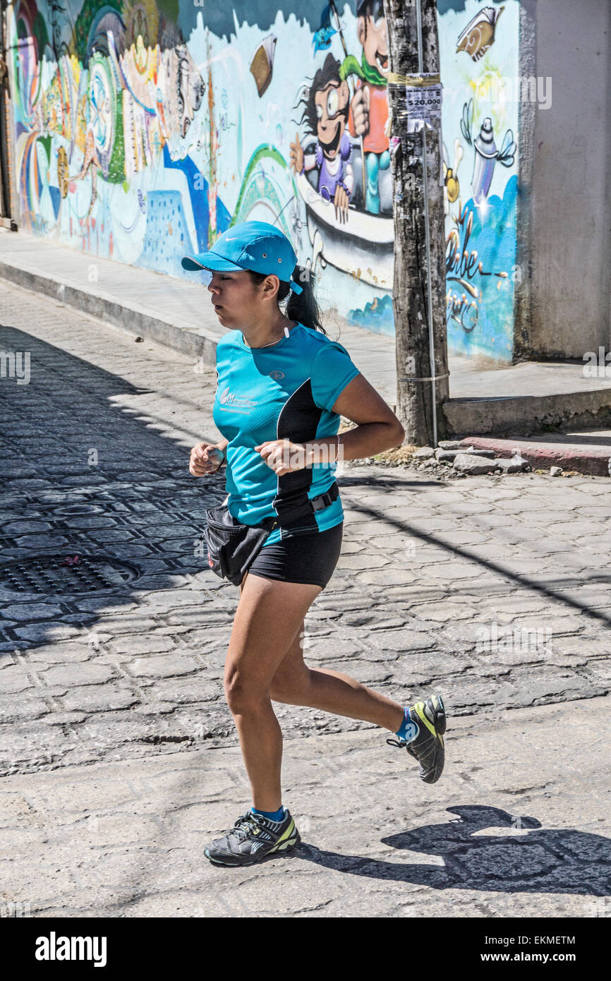 Déterminé young woman running à San Cristobal de las Casas demi-marathon passe coin de rue avec murale colorée Chiapas Banque D'Images