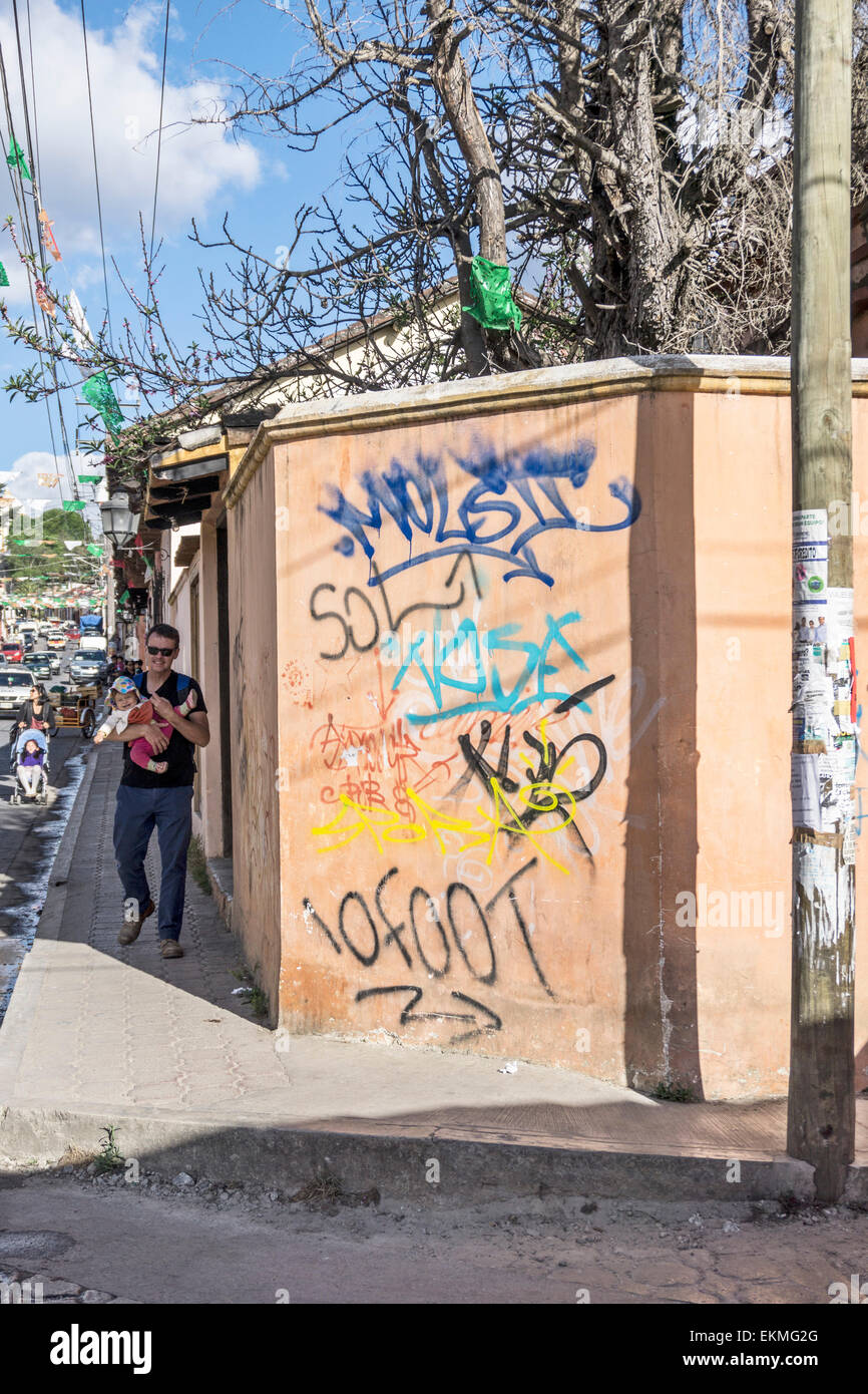 Graffiti sur mur à coin de rue avec amusé jeune père approcher tortiller holding baby girl San Cristobal de las Casas Banque D'Images