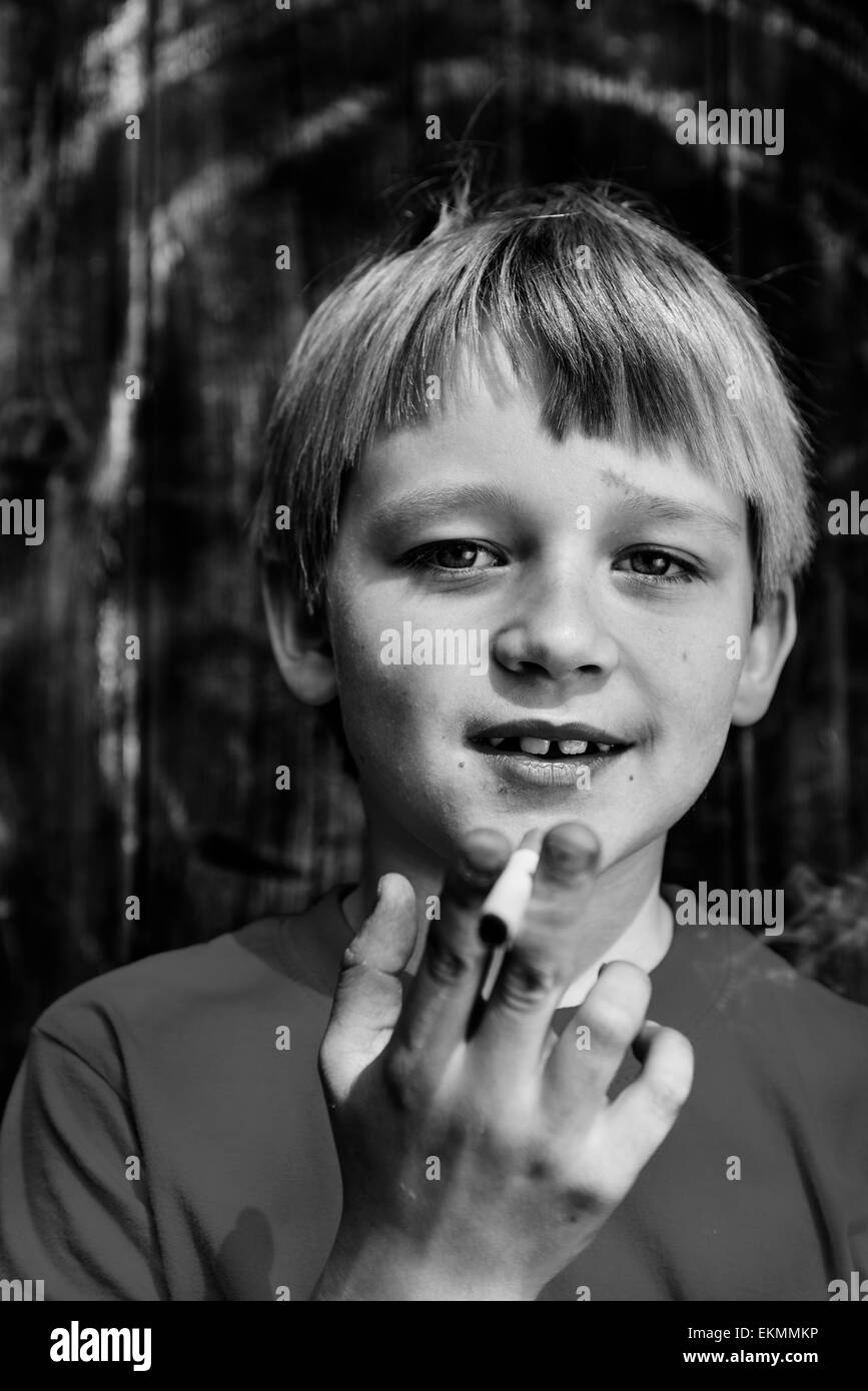 Portrait d'enfant garçon blond cigarette avec fond en bois sombre derrière lui Banque D'Images