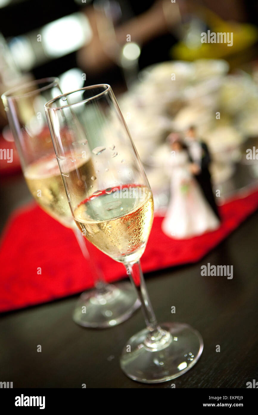 Deux verres de champagne à table avec Bride and Groom figure en plastique en arrière-plan montrant un événement de mariage. Banque D'Images