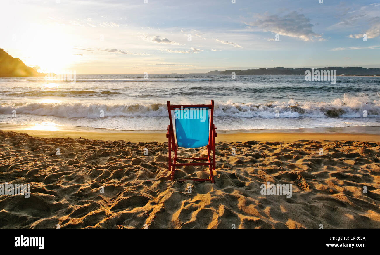Une chaise de plage sur le sable et un coucher de soleil sur l'horizon. Banque D'Images