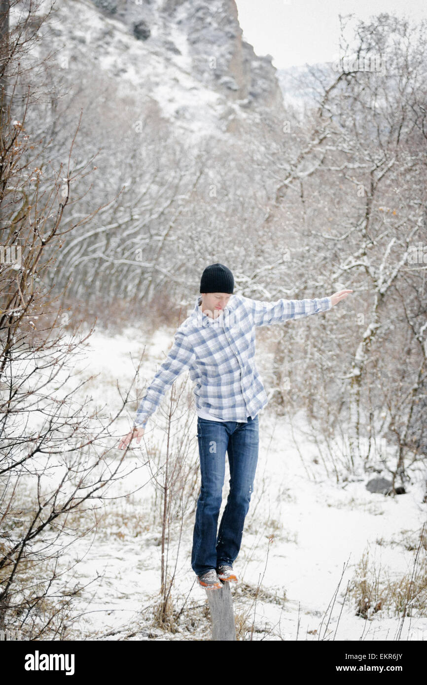 Un homme dans les montagnes en hiver, en équilibre sur un poteau de bois dans les forêts. Banque D'Images