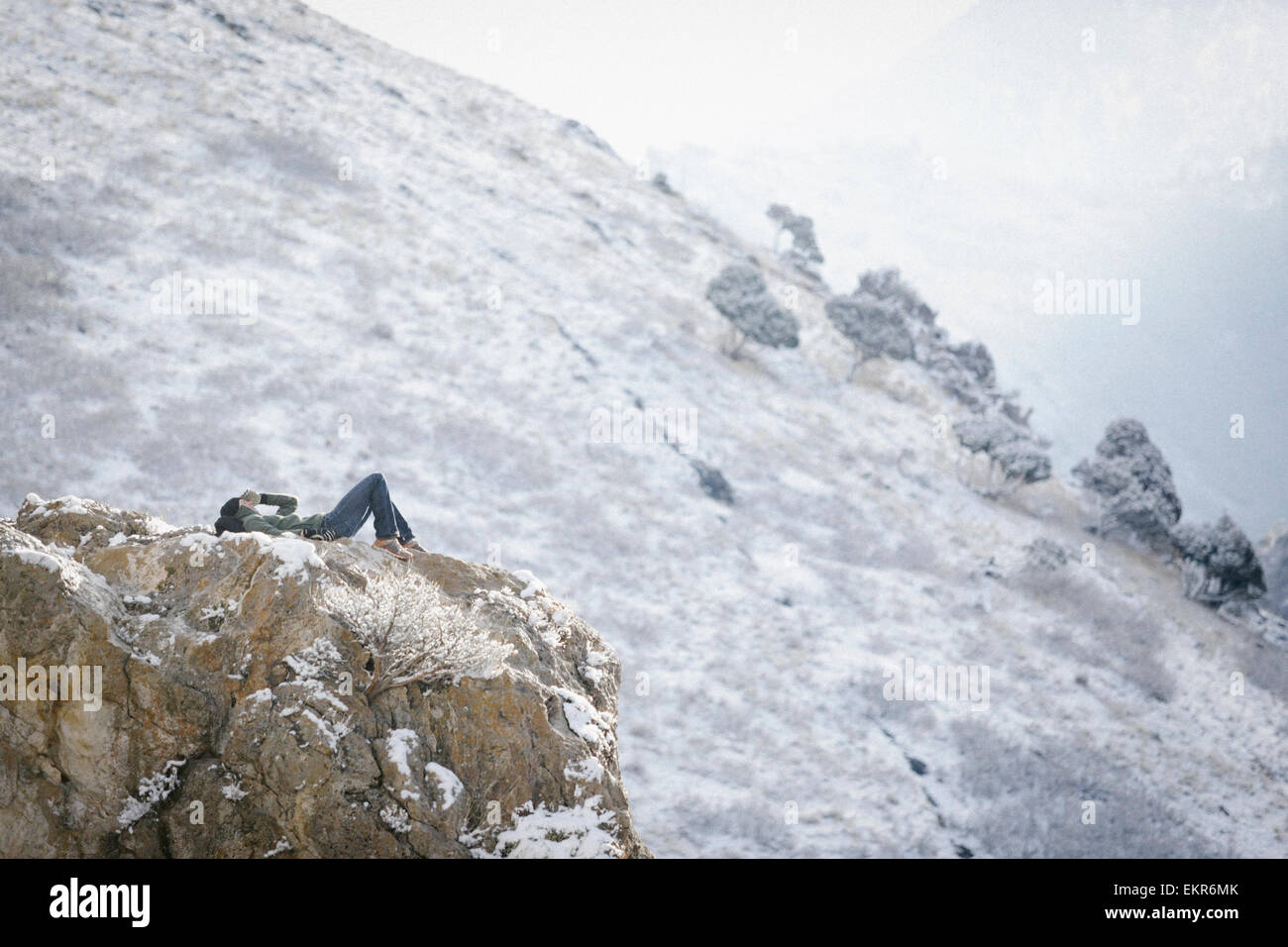 Un homme, un randonneur en montagne, prendre du repos couché sur un affleurement rocheux au-dessus d'une vallée. Banque D'Images