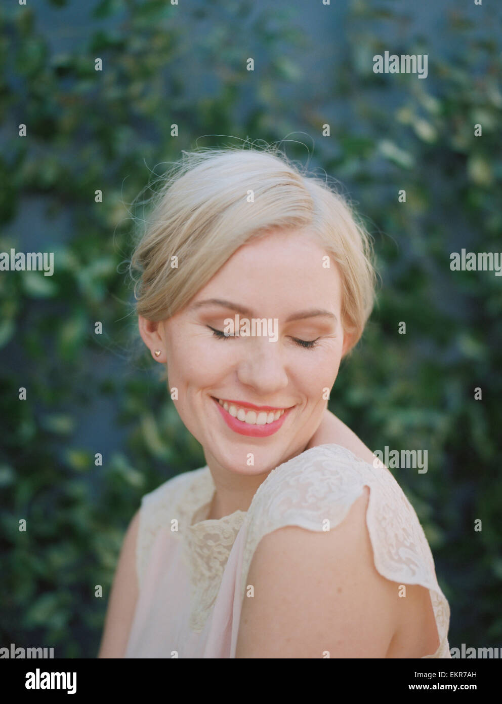 Une femme dans une robe en dentelle crème souriant avec ses yeux fermés. Banque D'Images