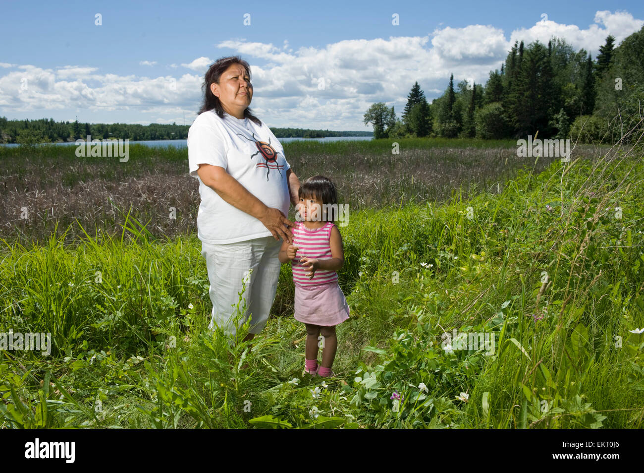 Grand-mère autochtone debout dans un champ à côté d'un lac avec sa petite-fille dans la région de Shoal Lake, Ontario, Canada. Banque D'Images