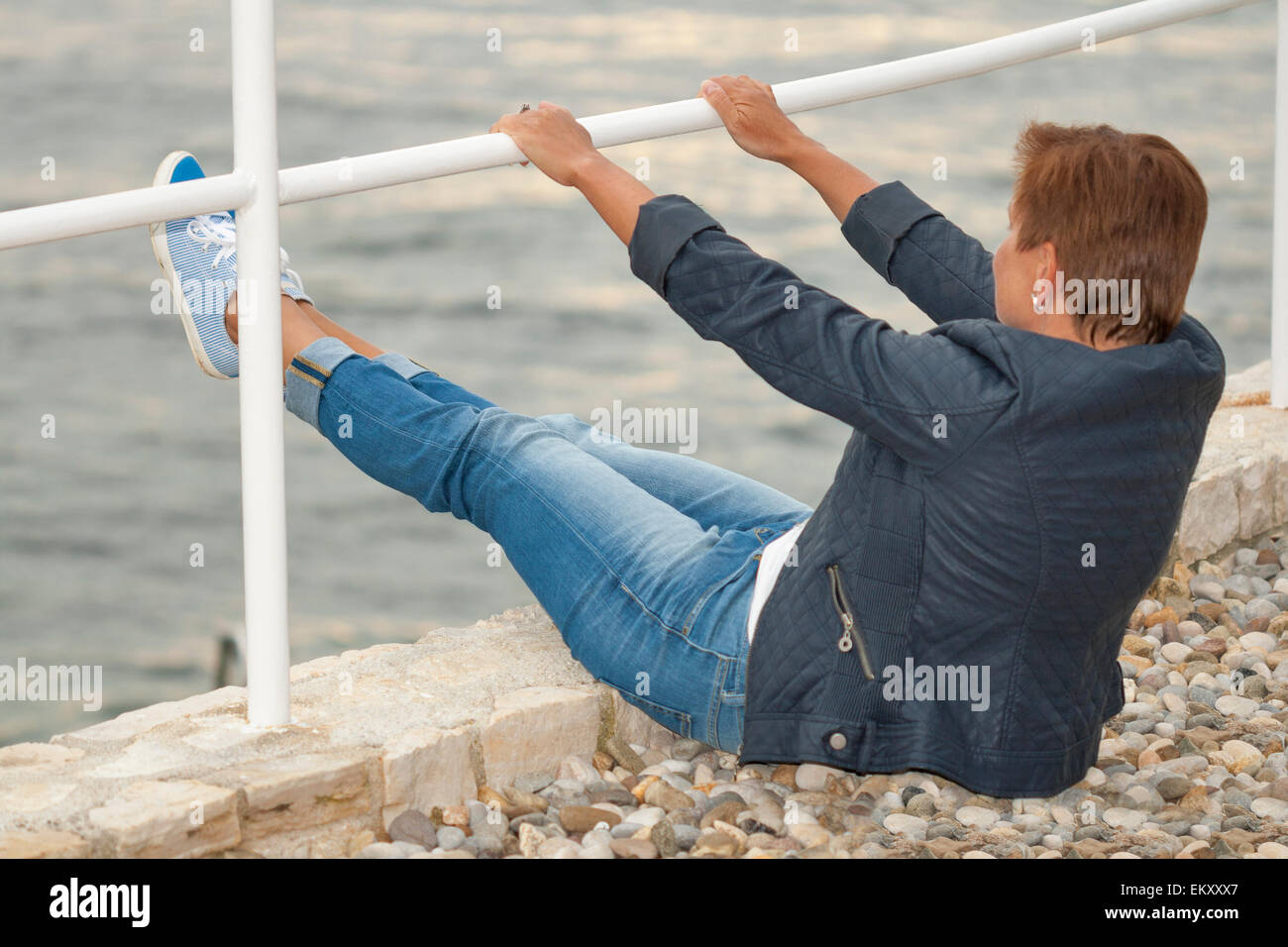 Middle aged woman femme bronzée en automne vêtements assis sur la plage de la mer de rochers Banque D'Images