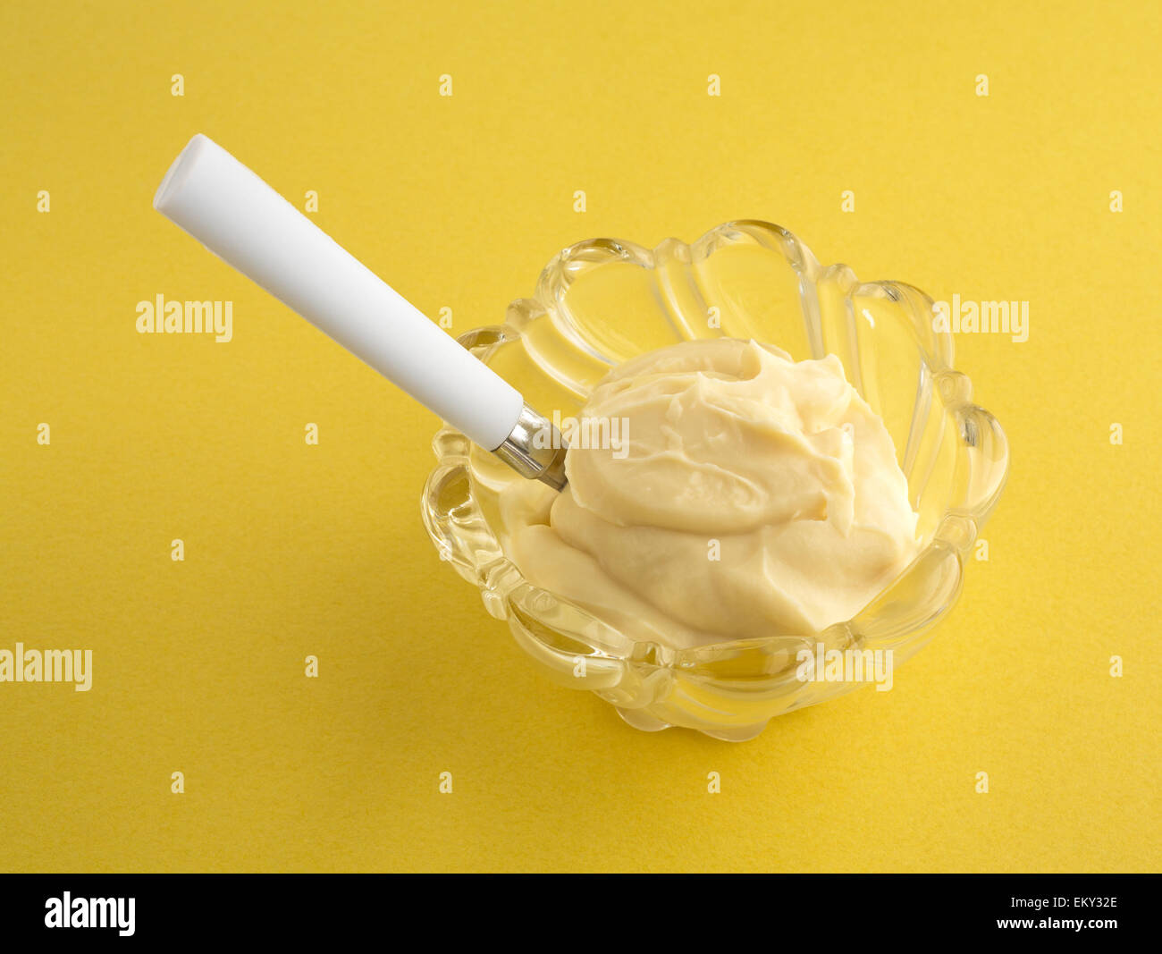 Un bol en verre décoratif avec une portion de pudding de vanille et une cuillère sur un fond jaune. Banque D'Images
