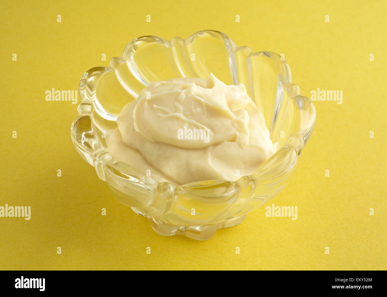Un bol en verre décoratif avec une portion de pudding de vanille sur un fond jaune. Banque D'Images
