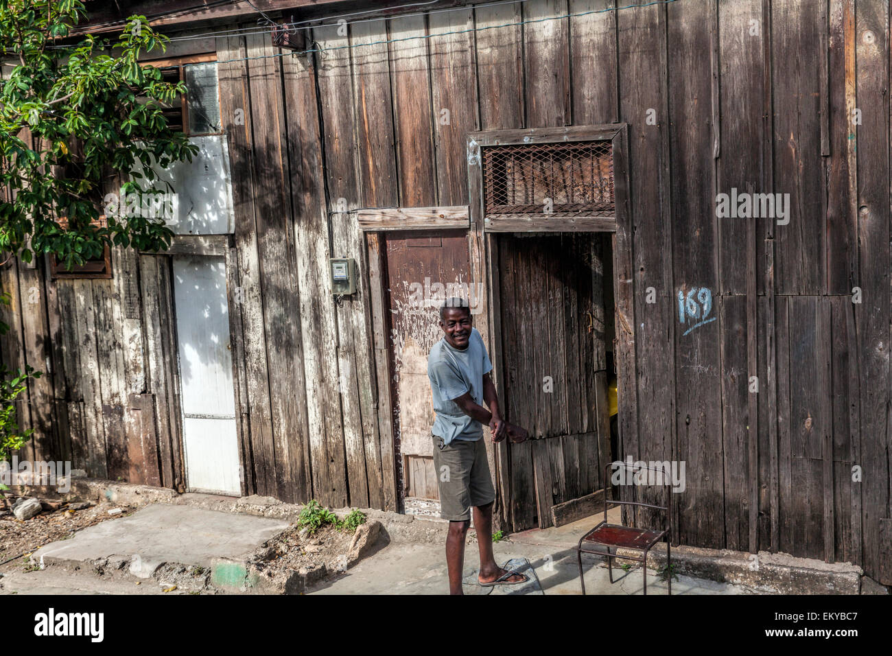 Homme cubain se tient à la porte de sa maison en bois près de la voie de chemin de fer et il s'intéresse aux passagers sur le train passé. Banque D'Images