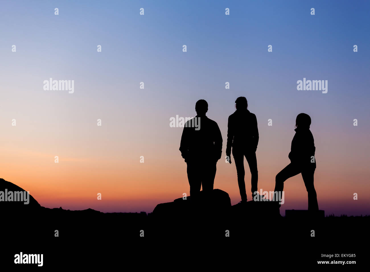 Silhouette d'une famille heureuse avec bras levés contre beau ciel coloré. Coucher du soleil d'été. Paysage Banque D'Images