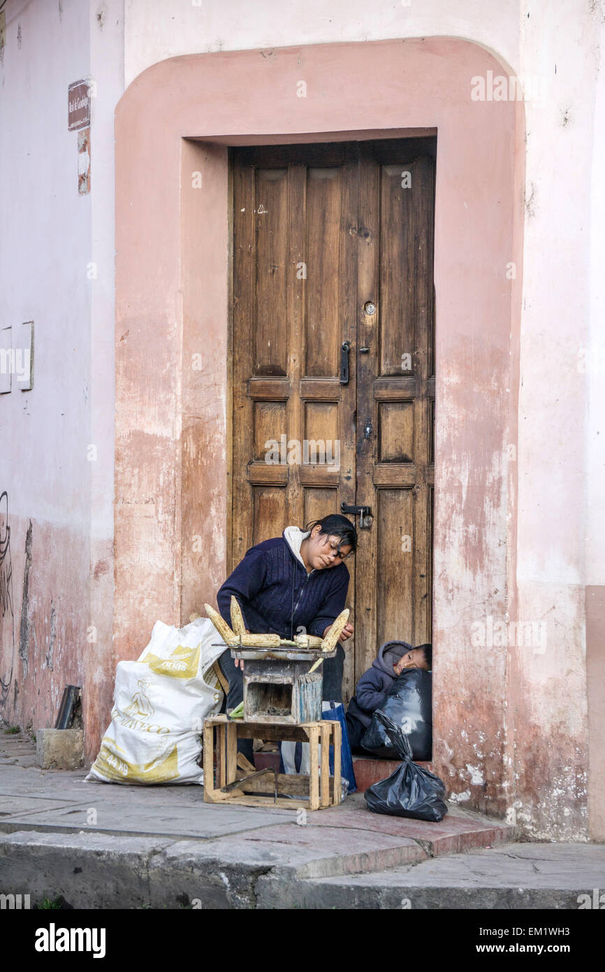 Les indiens mexicains des barbecues femme l'alimentation de rue de maïs sur trottoir comme son petit fils pan dans la porte San Cristobal de las Casas Banque D'Images