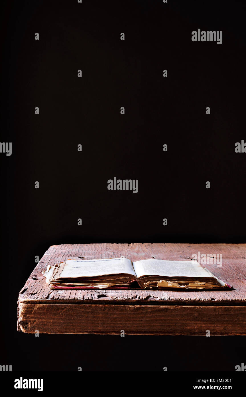Un vieux livre ouvert sur une table en bois rustique, sur un fond noir Banque D'Images