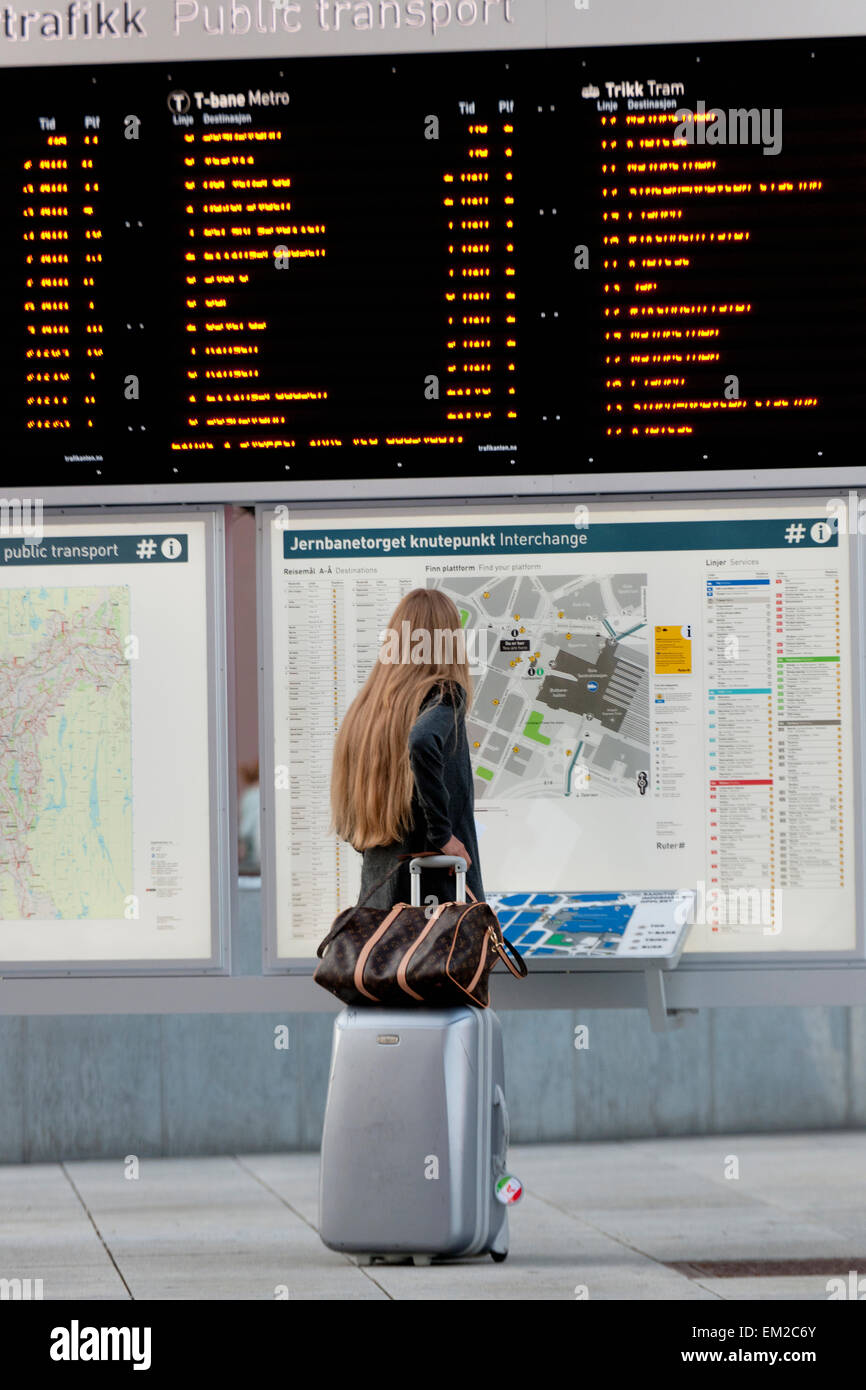 Une femme se tient avec ses bagages à la recherche à la carte des routes de transport public ; Oslo Norvège Banque D'Images