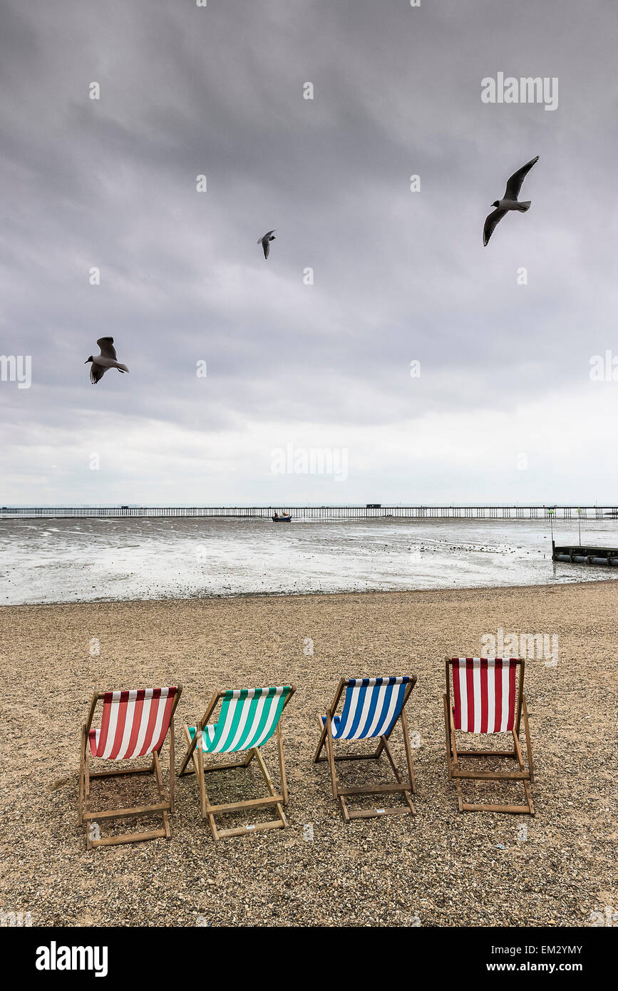 Vol de mouettes au-dessus des chaises vides sur la plage de Jubilee à Southend sur un jour nuageux. Banque D'Images