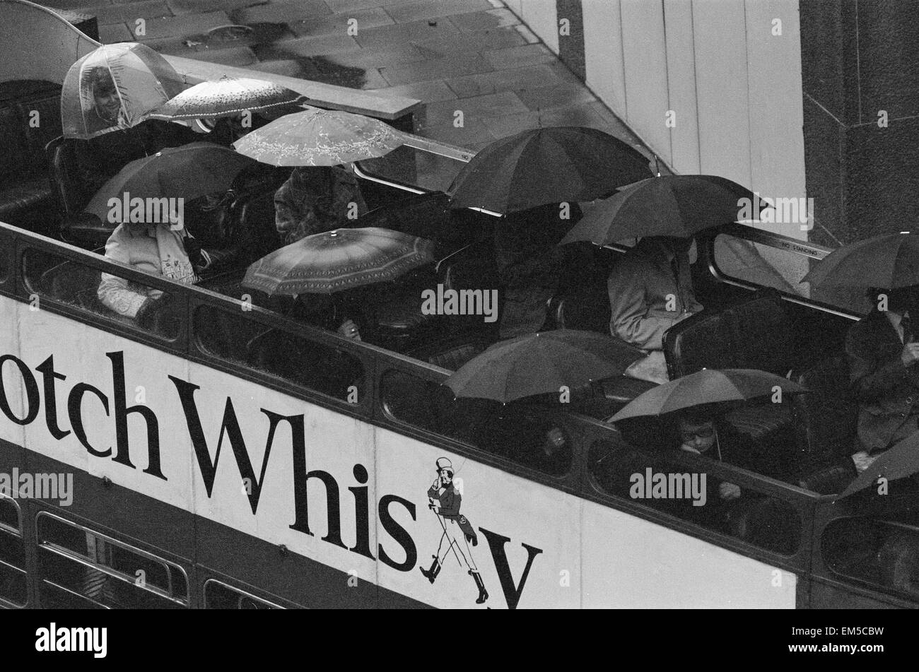 Les touristes s'asseoir sous leur parapluie sur le pont supérieur d'un bus à toit ouvert au cours d'une visite touristique de Londres sous la pluie. 28 octobre 1976. Banque D'Images