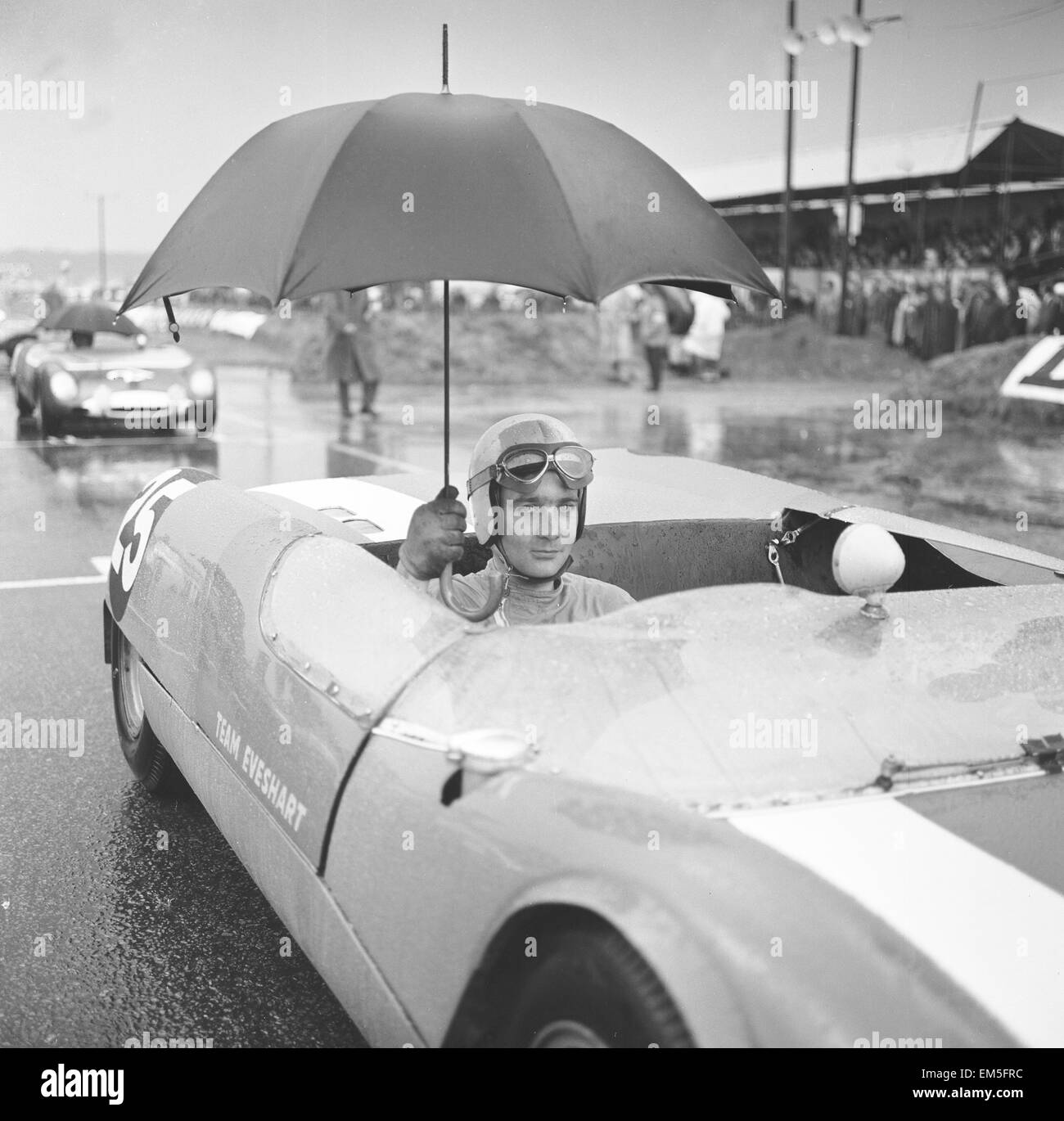 Brian Hart est titulaire d'un parapluie jusqu'à marcher sur les fortes pluies qu'il attend pour le début de la course de 3 heures dans sa Lotus 23b à Snetterton le 27 septembre 1964 Banque D'Images