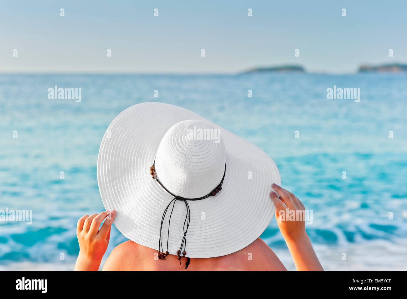 Une femme en train de bronzer sur une chaise longue sur la plage et tenir la main hat Banque D'Images