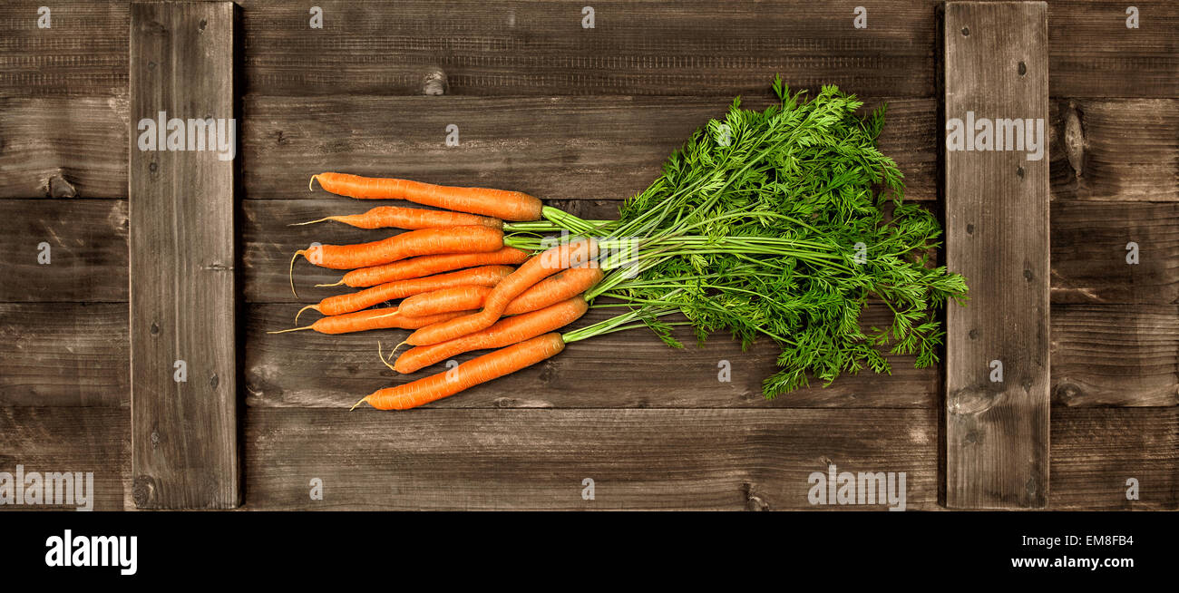 La carotte fraîche avec des feuilles vertes mûrs sur fond de bois. Légume. Concept alimentaire. Retro style tonique photo Banque D'Images