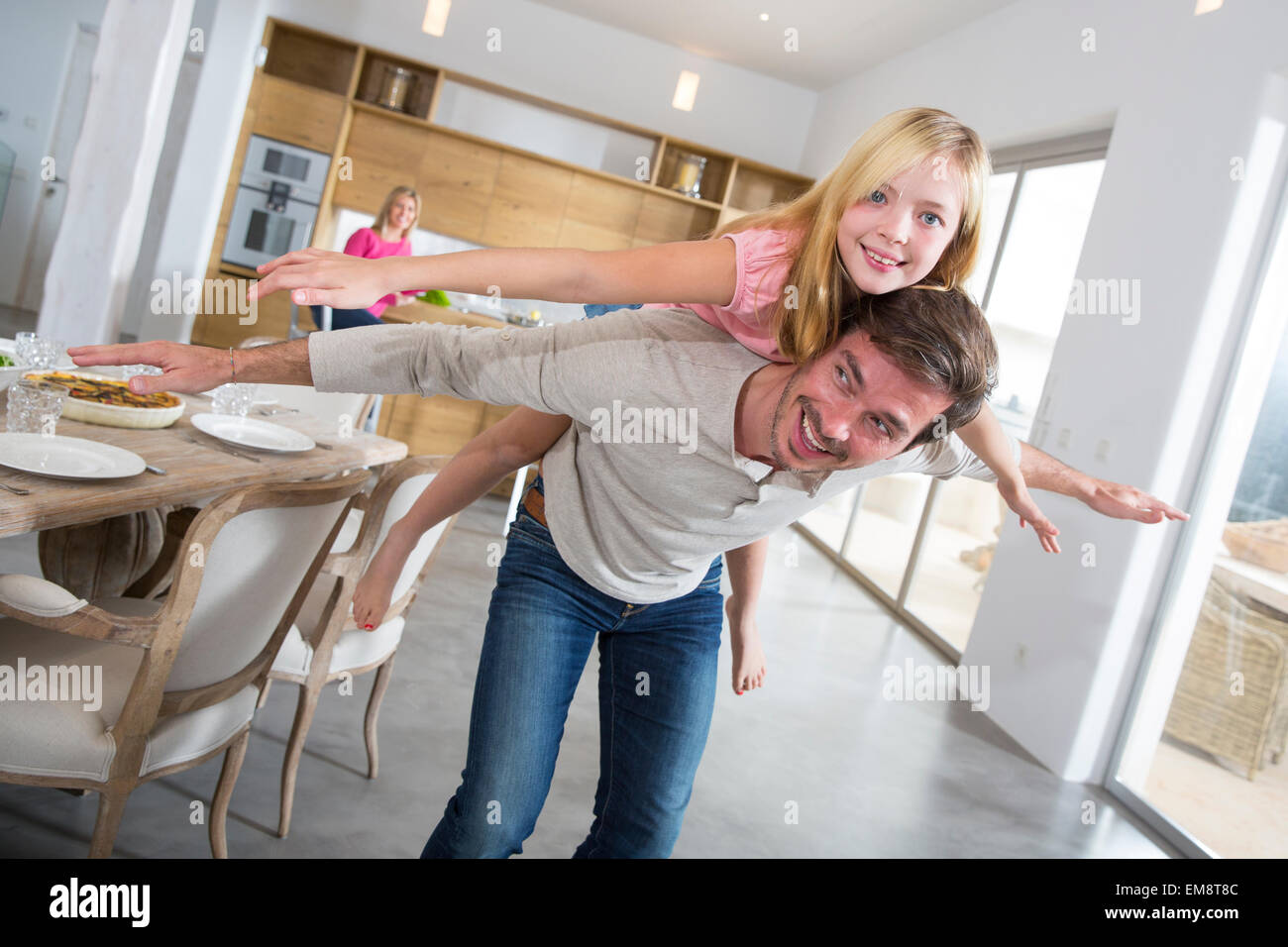 Man giving daughter piggy back in dining room Banque D'Images