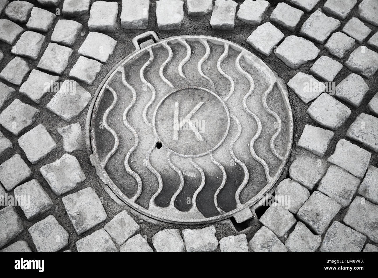 Trappe ronde en milieu urbain chaussée de pierre avec grande lettre K Banque D'Images