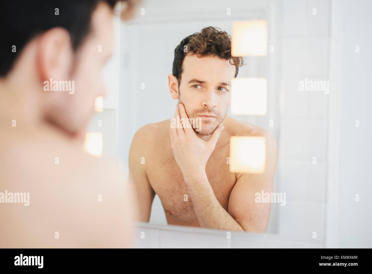 Jeune homme contrôler son visage en miroir de salle de bains Banque D'Images