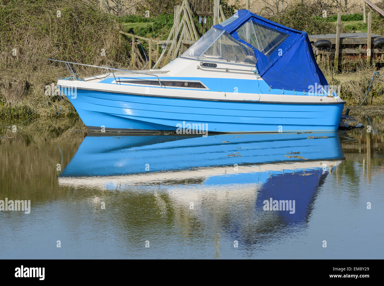 Petit plaisir bleu bateau amarré sur une rivière avec son reflet dans l'eau. Banque D'Images