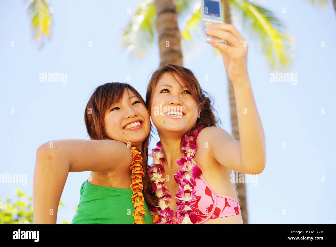 Deux japonais pour prendre une photo d'elles avec un téléphone appareil photo, des palmiers derrière Banque D'Images