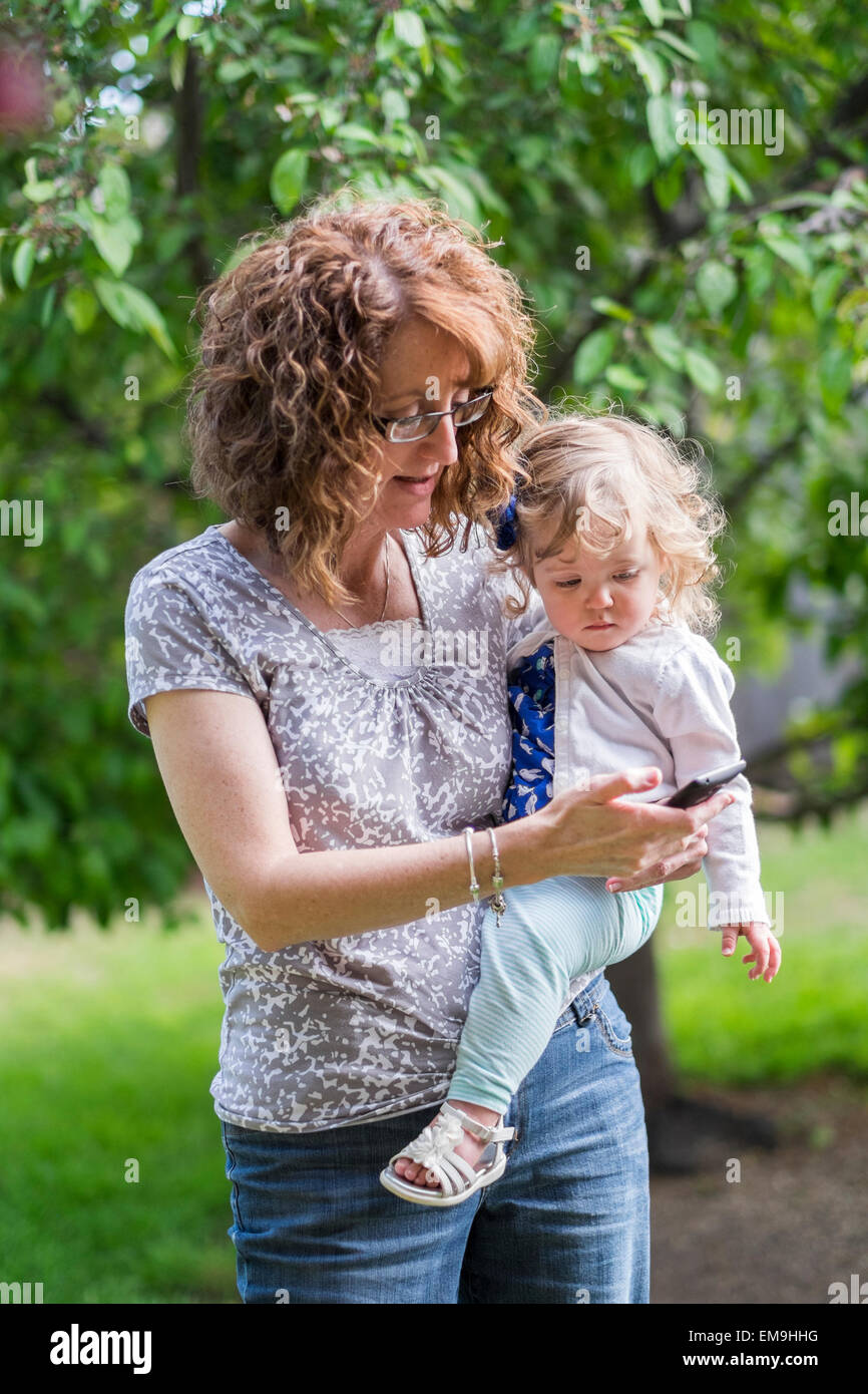 Une grand-mère âgée de 50 ans tient son enfant petite-fille sur sa hanche tout en plaçant un appel mobile à l'extérieur. Banque D'Images