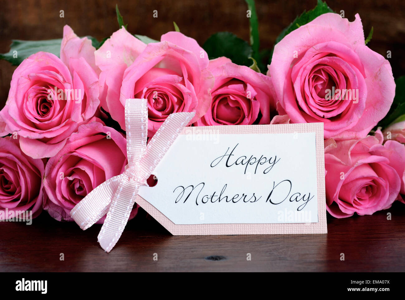 Roses roses Fête des mères sur la table rustique en bois sombre avec étiquette-cadeau de vœux, libre. Banque D'Images