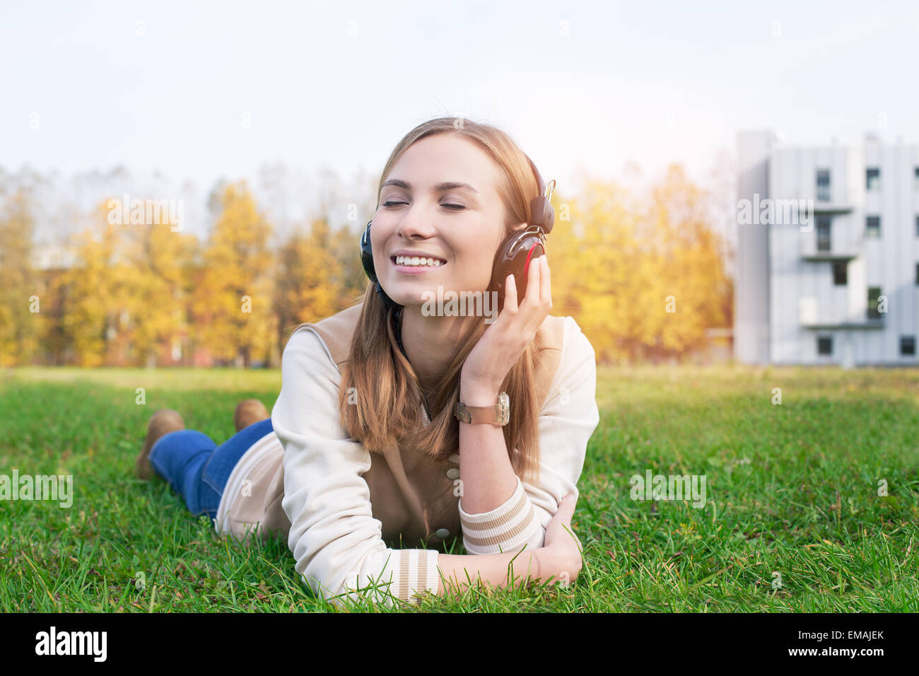 Student lying on Green grass et l'écoute de la musique dans des écouteurs avec les yeux fermé Banque D'Images