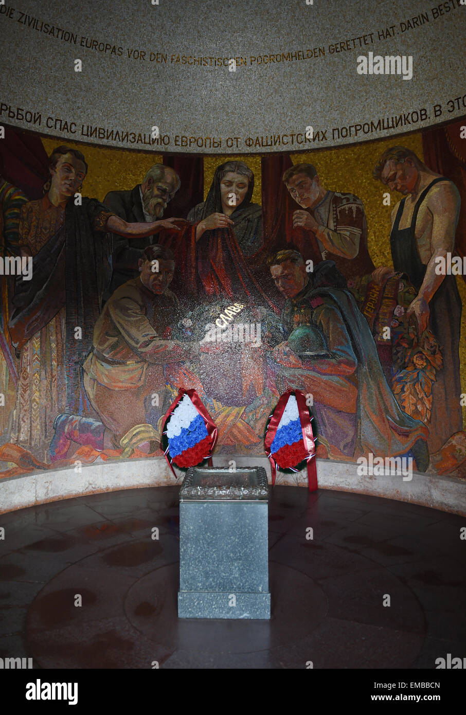 Berlin, Allemagne. 10 avr, 2015. Le pavillon du Soviet War Memorial de Treptower Park avec une mosaïque, une fédération de l'inscription, la traduction en allemand, russe et de drapeaux fleurs à Berlin, Allemagne, 10 avril 2015. La colline et le pavillon sont tombes slaves de la région de la rivière Don. Le mot russe 'SLawa' pour 'gloire' scintille à l'or. Le site a été présenté en mai 1949 et rend hommage aux soldats de l'Armée rouge qui est tombé dans la seconde guerre mondiale. Autour de 7 000 soldats tués dans la bataille de Berlin ont été enterrés ici. Photo : Jens Kalaene/dpa/Alamy Live News Banque D'Images