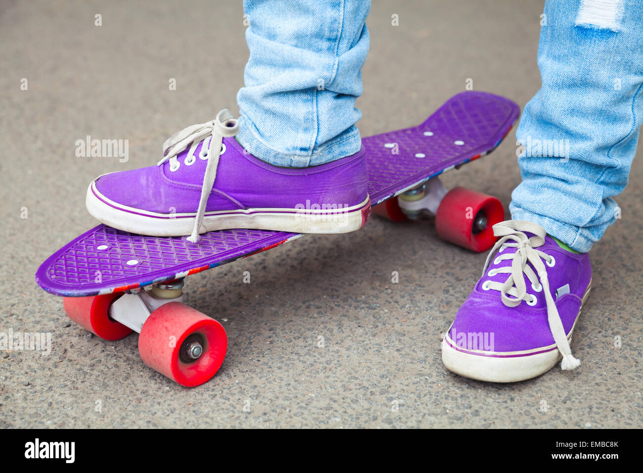 Les jeunes en jeans et gumshoes skateboarder béquilles. Close-up fragment de skateboard et les pieds Banque D'Images