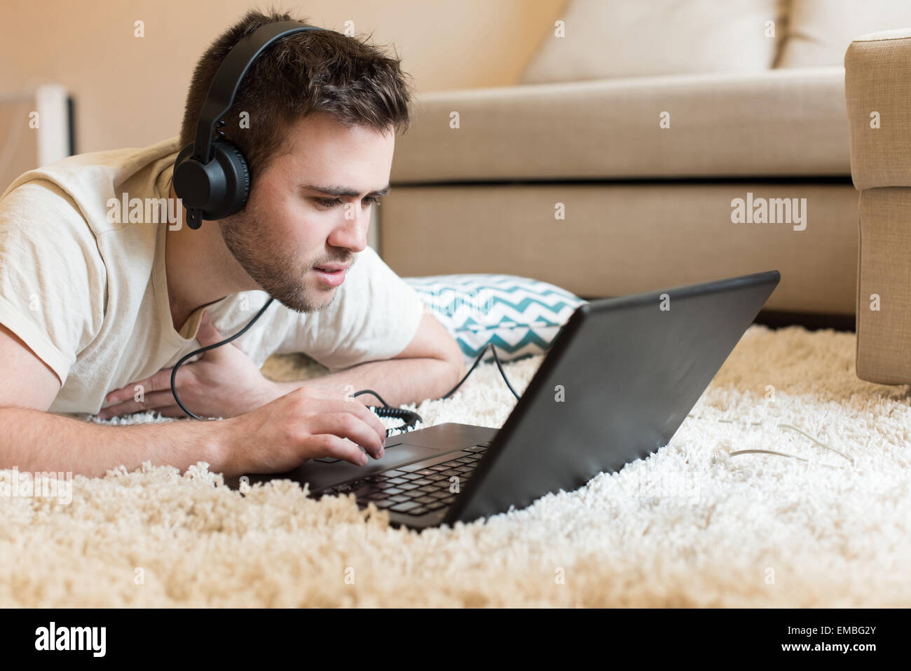 L'homme gisant sur le sol à l'aide de casque sur l'ordinateur portable Banque D'Images