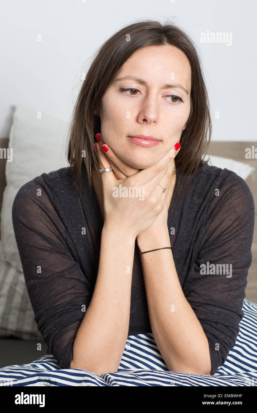 Mid-adult woman avec mal de gorge sitting in bed Banque D'Images
