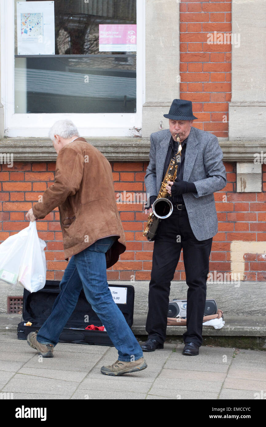 Un musicien ambulant de rue jouant un saxophone ténor comme un passant met l'argent dans son cas Banque D'Images
