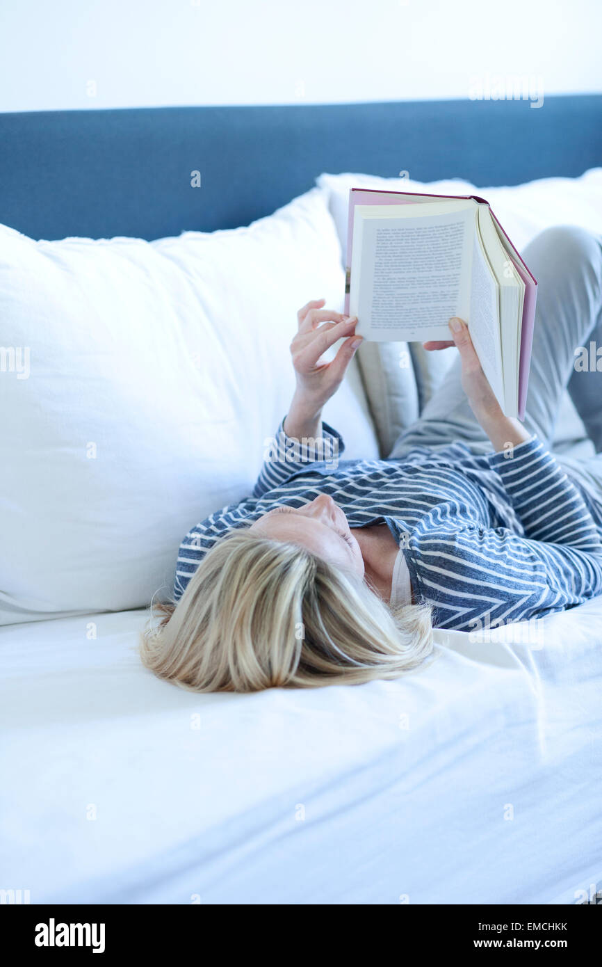 Woman lying on couch reading a book Banque D'Images