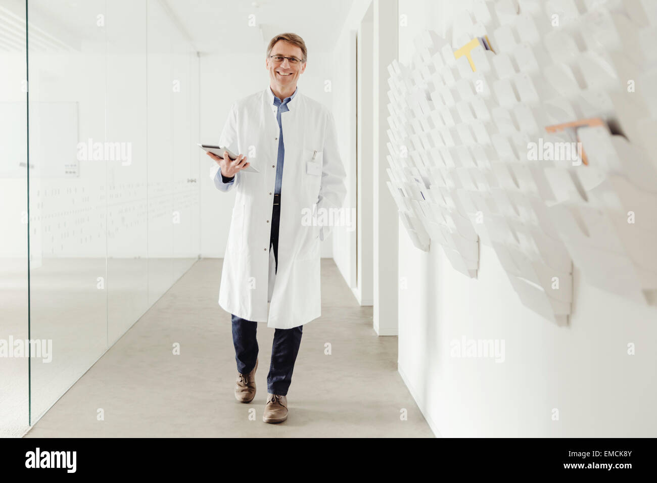 Smiling young man in lab coat walking in hallway Banque D'Images