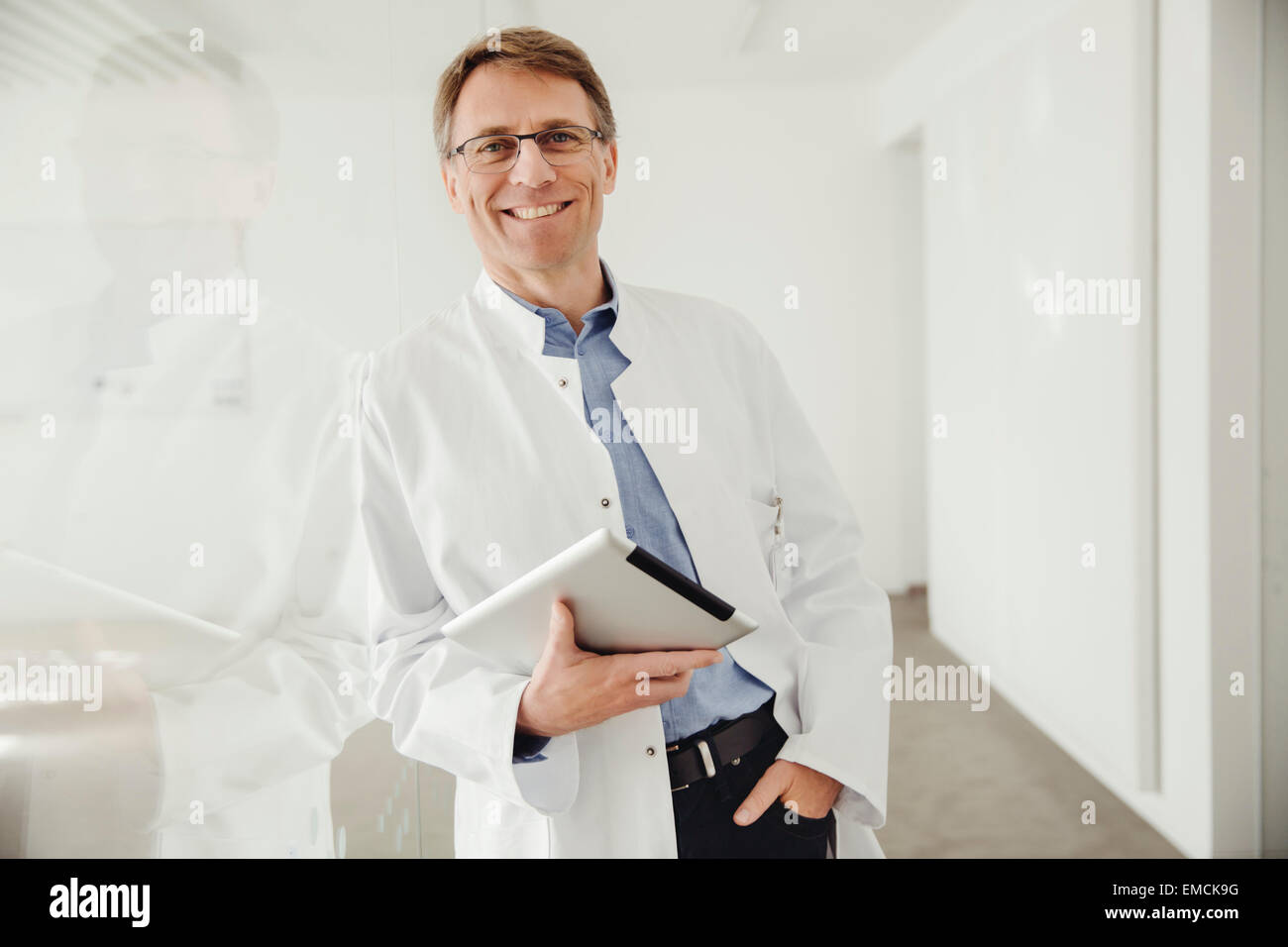 Smiling young man in lab coat holding digital tablet Banque D'Images