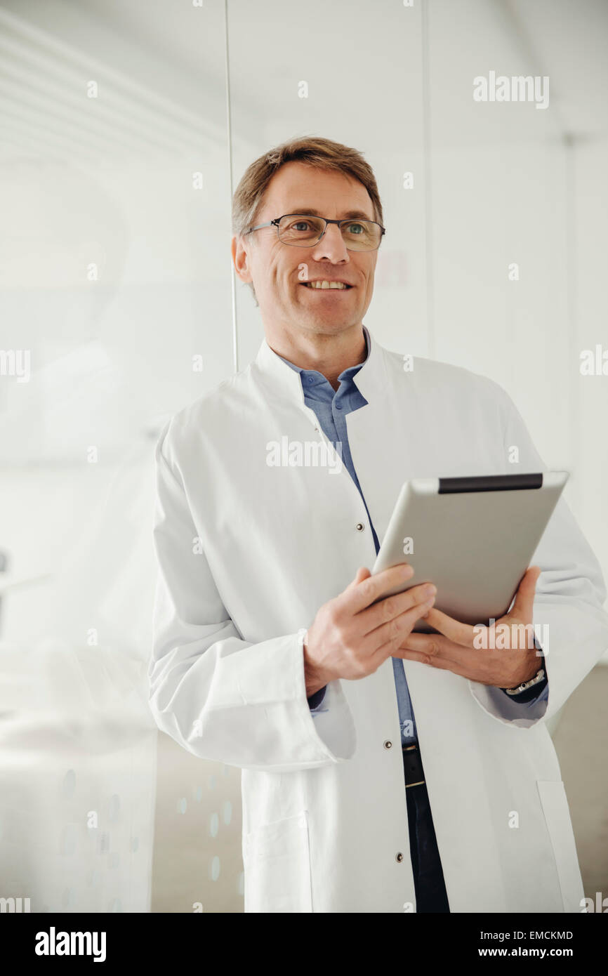 Smiling young man in lab coat holding digital tablet Banque D'Images