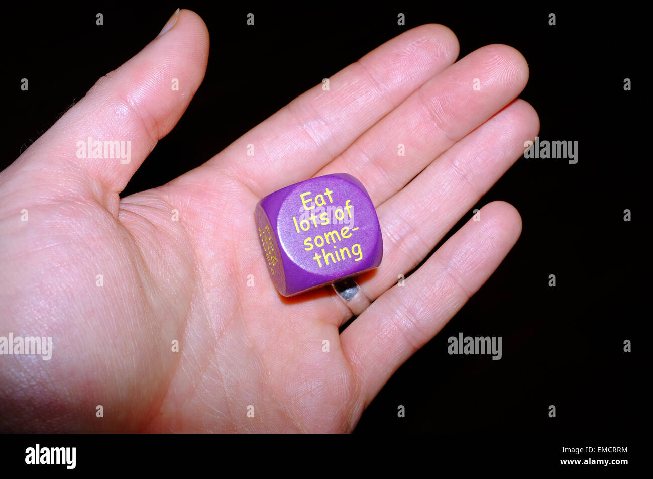 Une main blanche tenant une activité dés violet sur fond noir. Banque D'Images