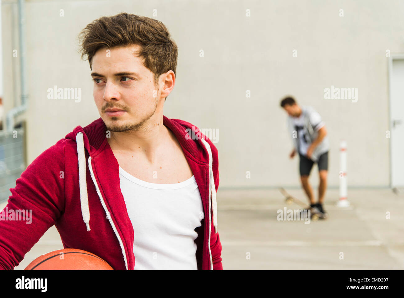 Deux jeunes hommes avec skateboard et basket-ball sur niveau parking Banque D'Images