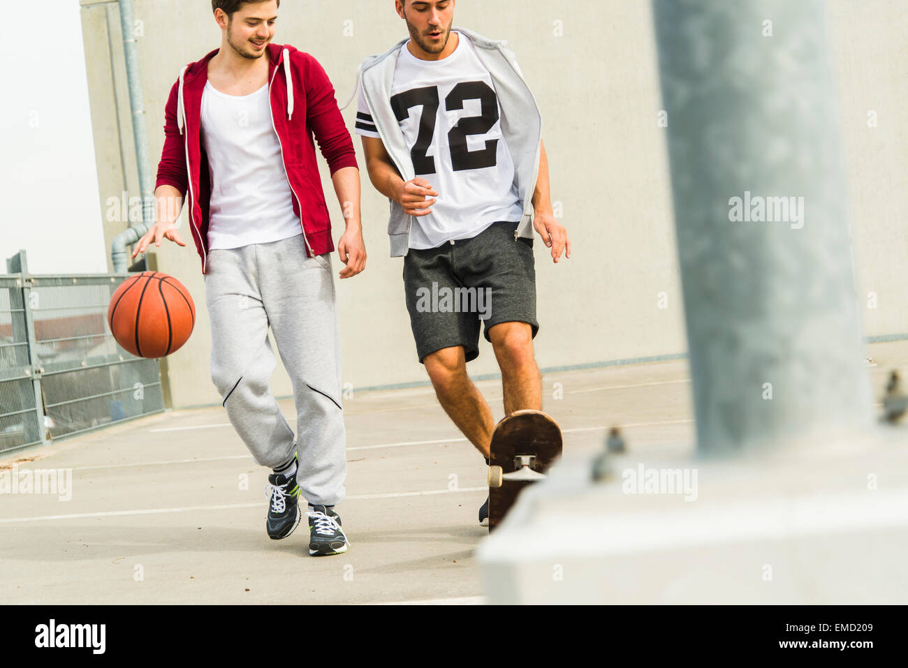 Deux jeunes hommes avec skateboard et basket-ball sur niveau parking Banque D'Images
