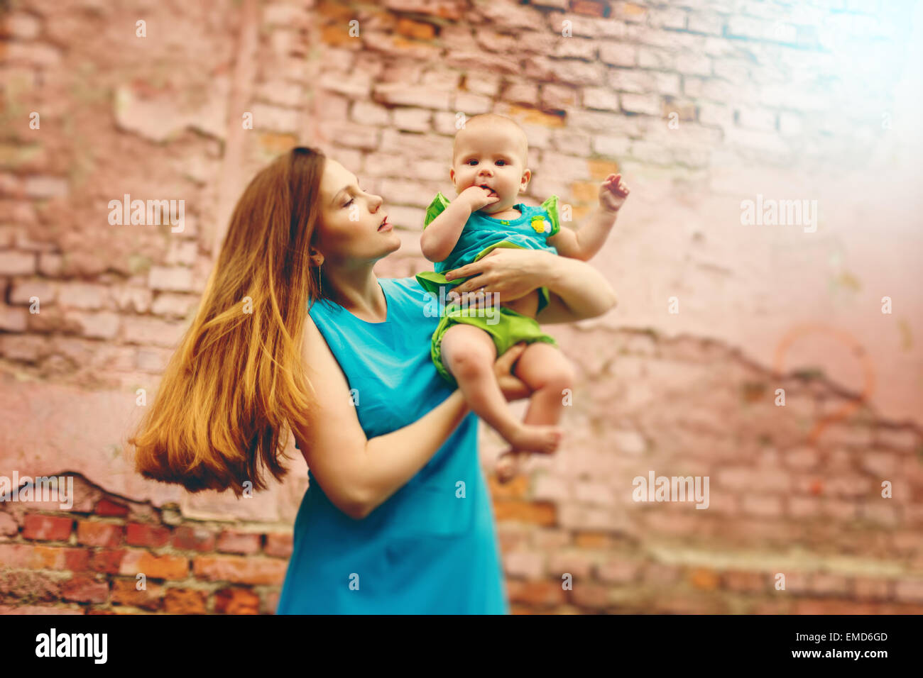 Belle jeune maman jouant avec son joli petit bambin contre mur de briques. Les tons de l'image avec des couleurs chaudes. Banque D'Images