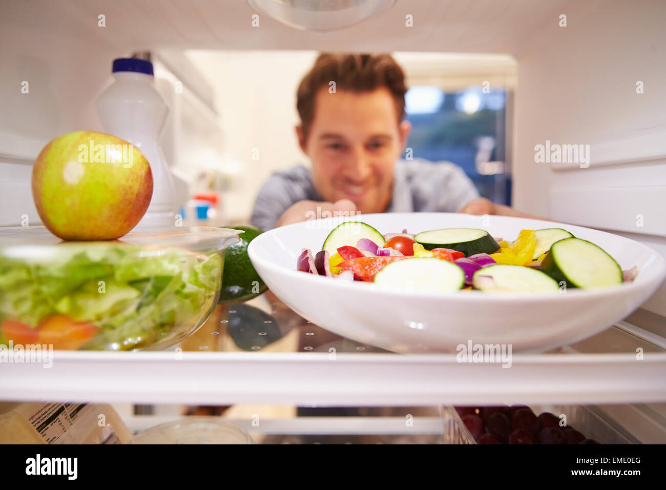 L'homme à l'intérieur d'un réfrigérateur plein de nourriture et en choisissant Salad Banque D'Images